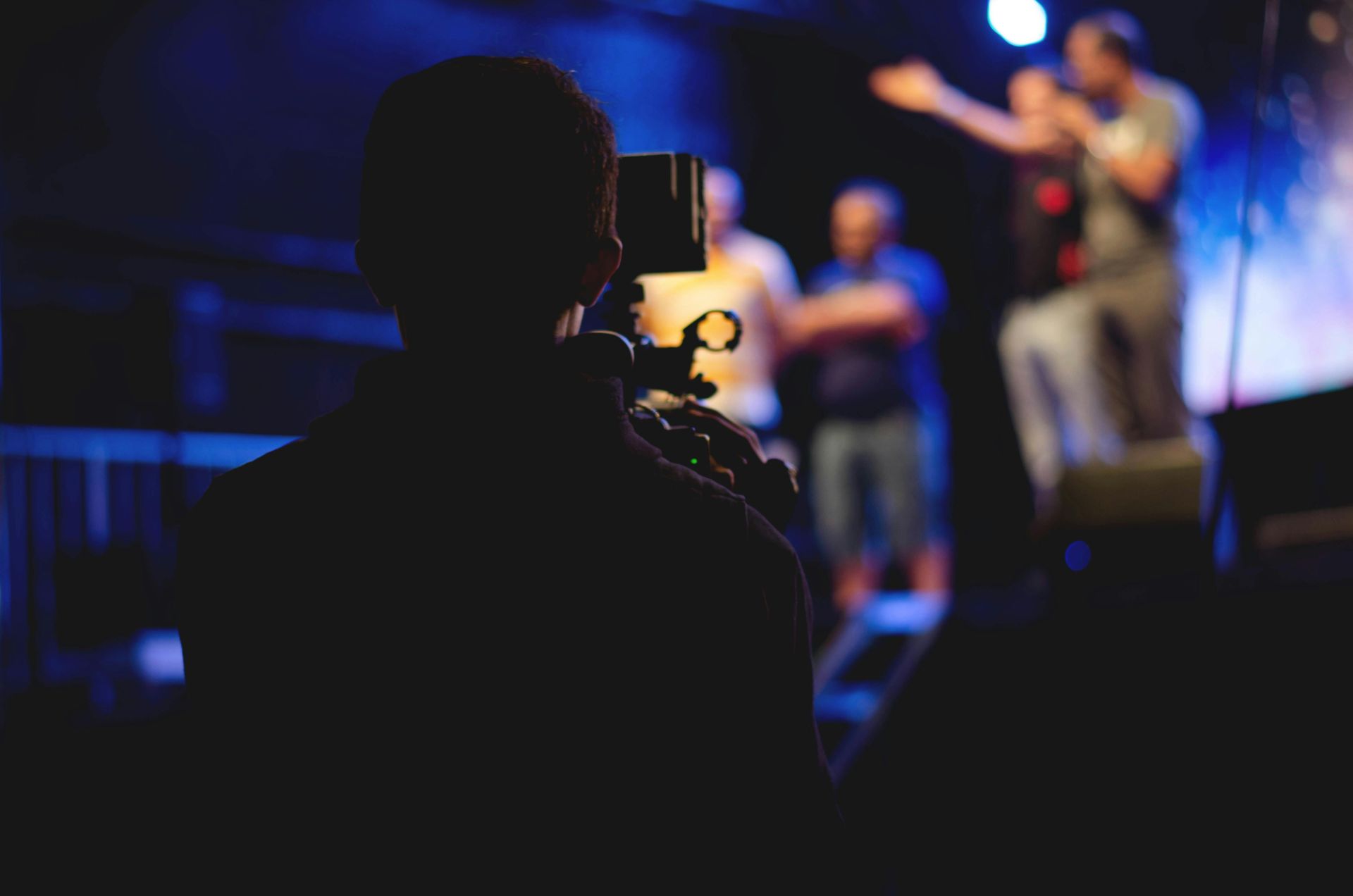 A cameraman films a live concert performance, capturing the dynamic stage action.